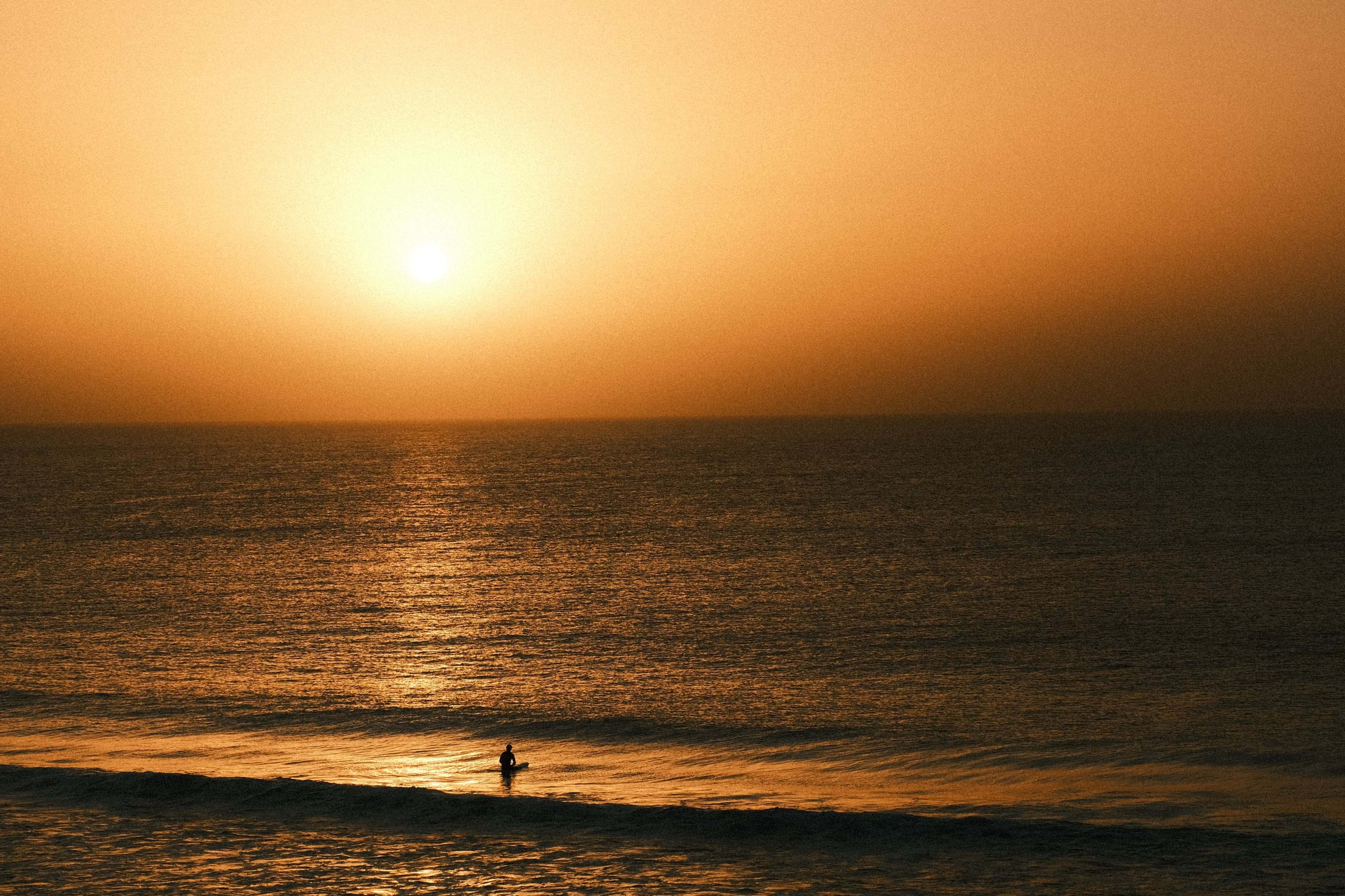 Surfista solo sentado en la tabla mientras el sol se pone sobre el Atlántico