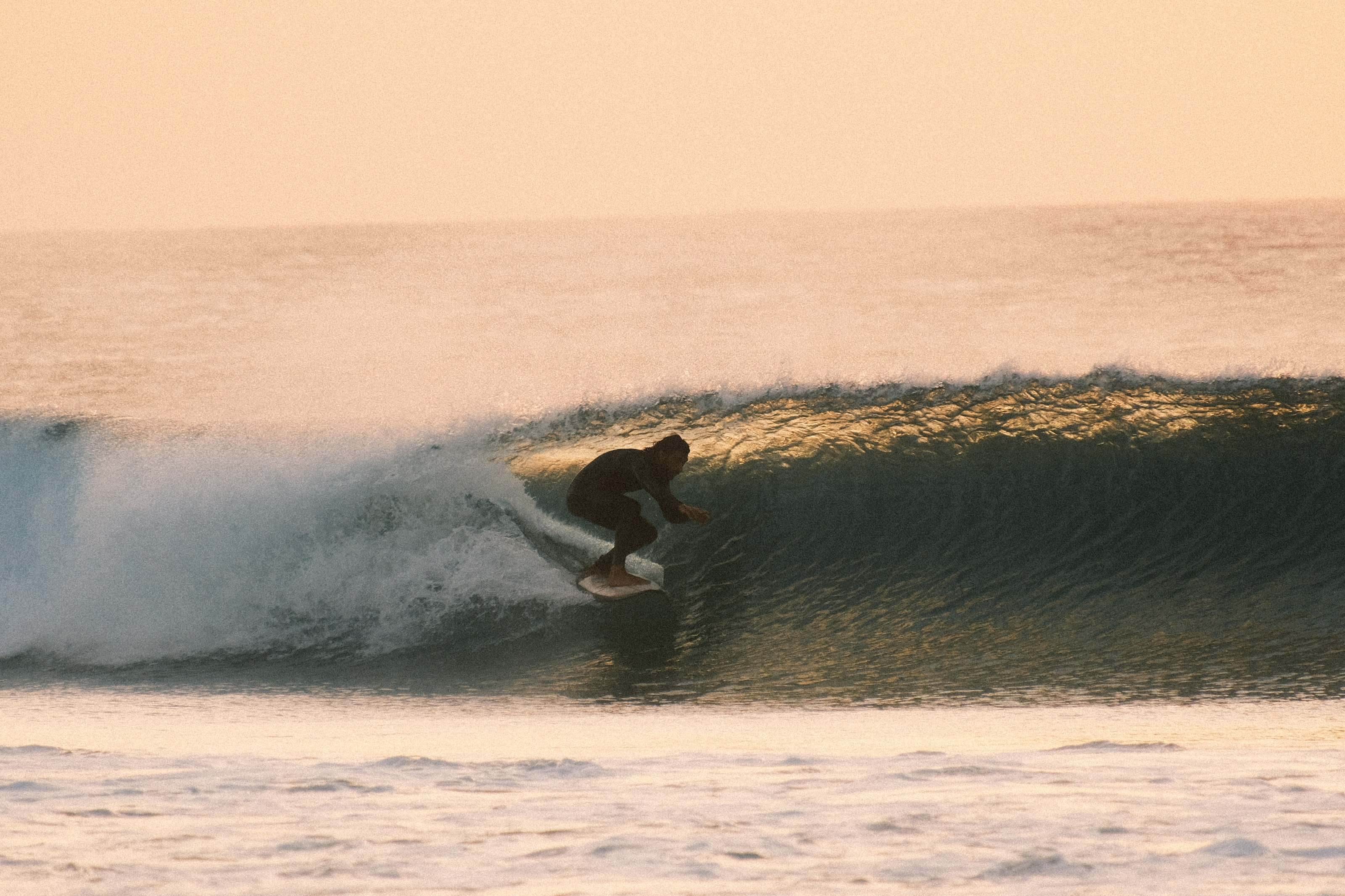 Surfista a contraluz entrando en un tubo dorado al atardecer en Fuerteventura