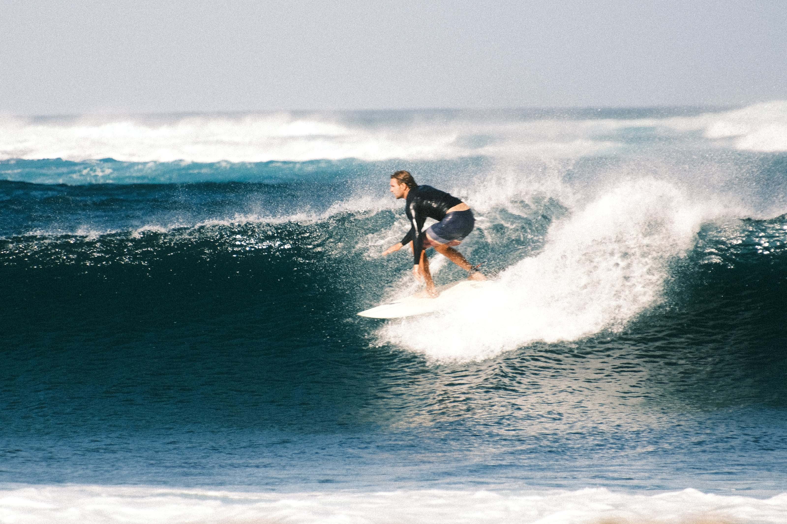 Surfista haciendo un bottom turn en una ola azul y potente en Fuerteventura