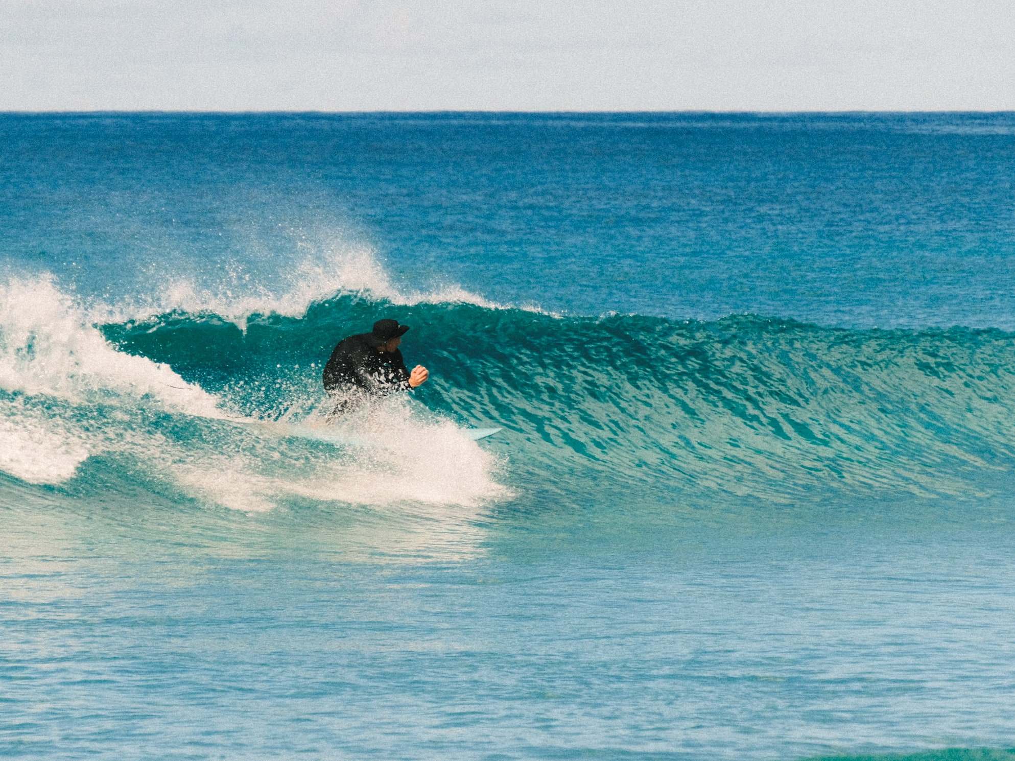 Surfista con gorra bajando una pared turquesa en Fuerteventura
